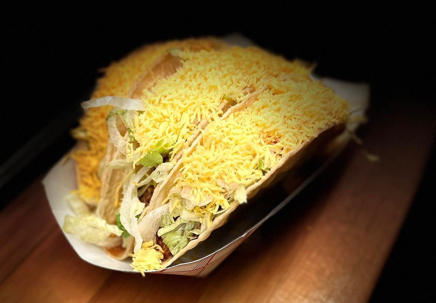 A taco with cheese and lettuce is sitting on a wooden table.