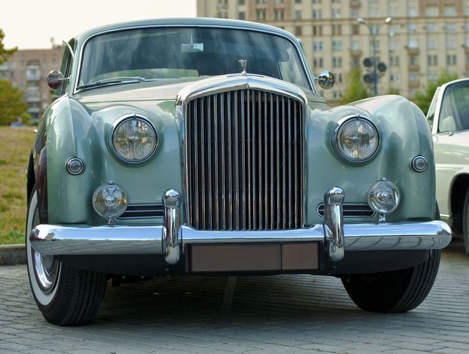 A green rolls royce bentley is parked in a parking lot.