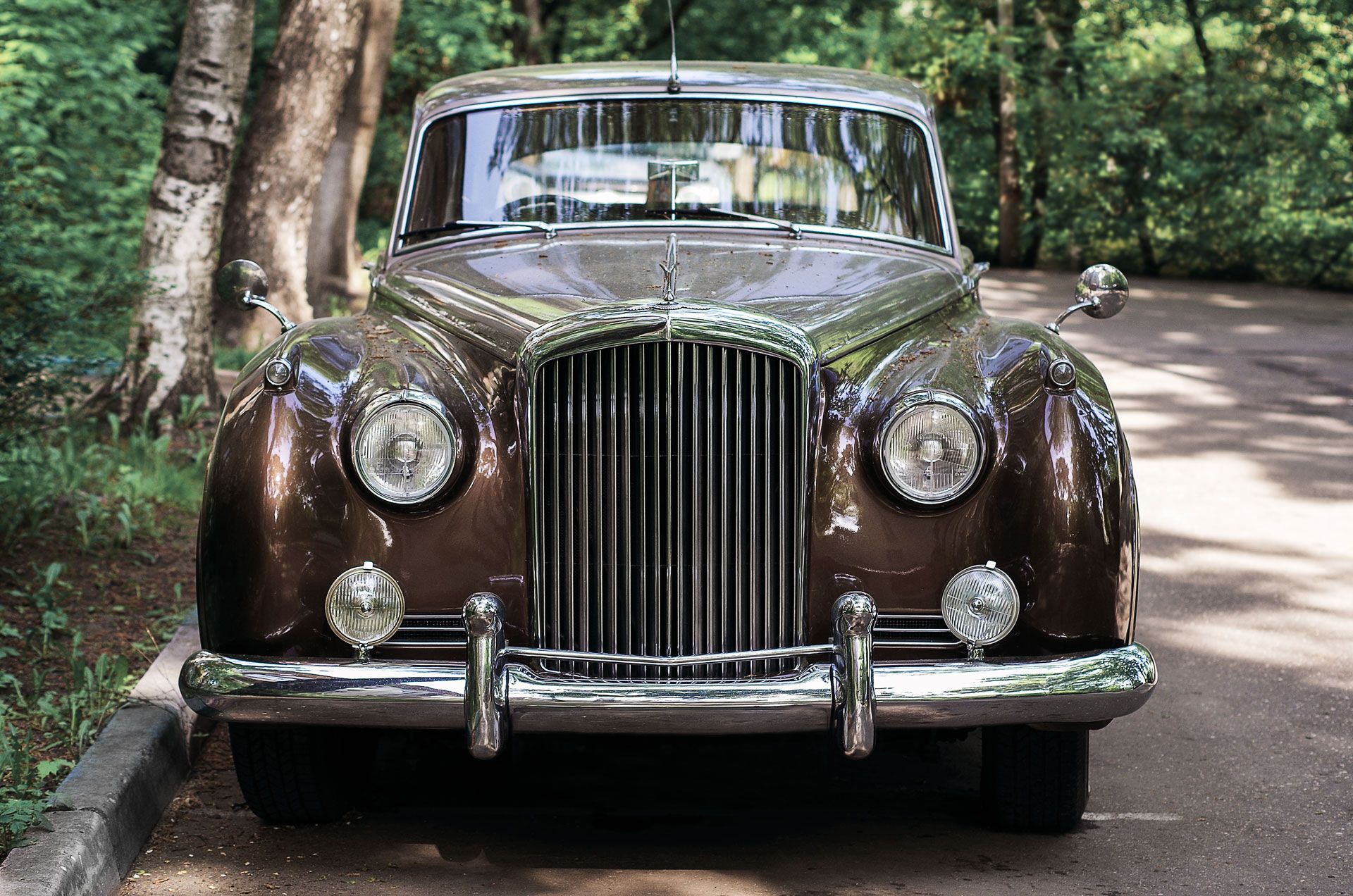 An old brown car is parked on the side of the road