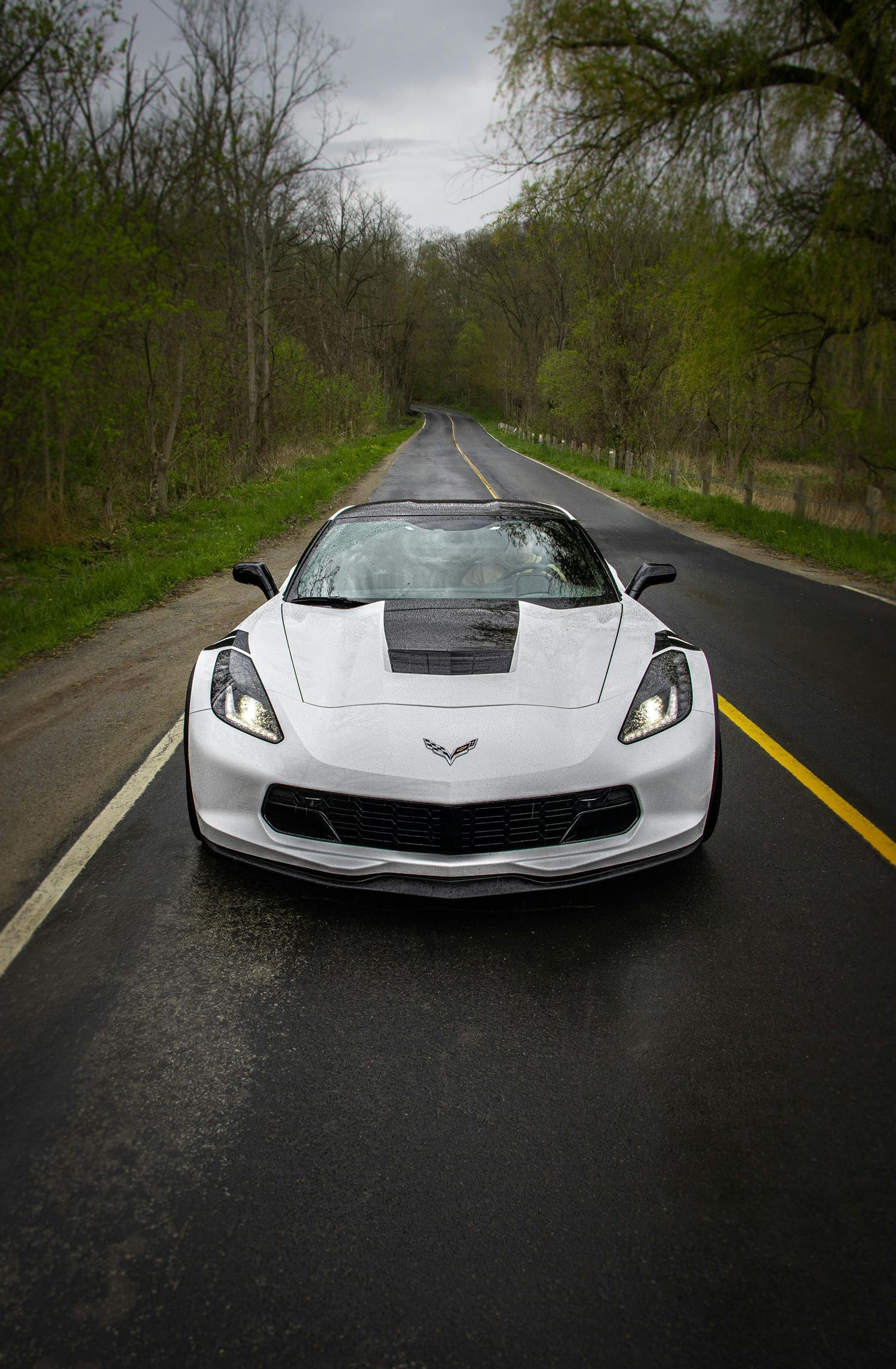 A white sports car is driving down a country road.