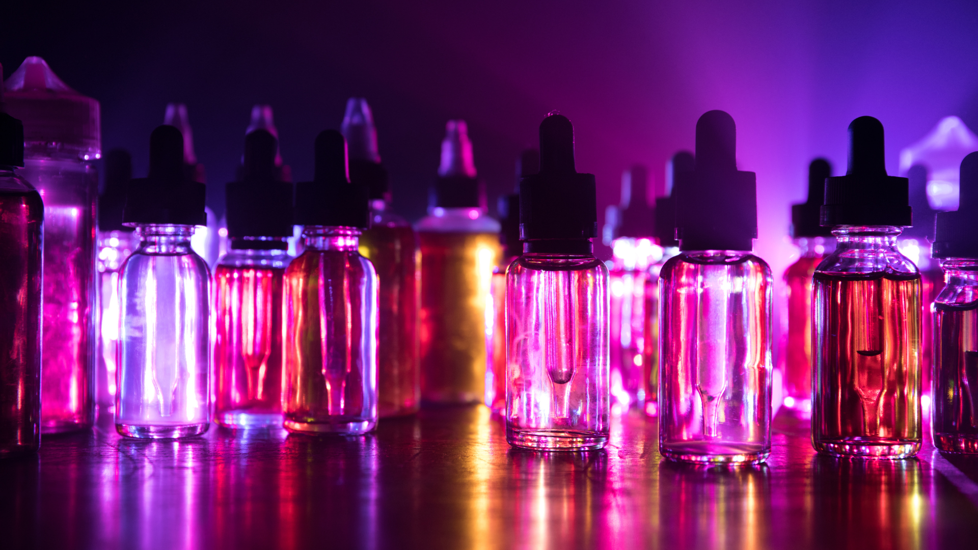 A row of small dropper bottles filled with colorful liquids glowing under purple and orange stage lighting.