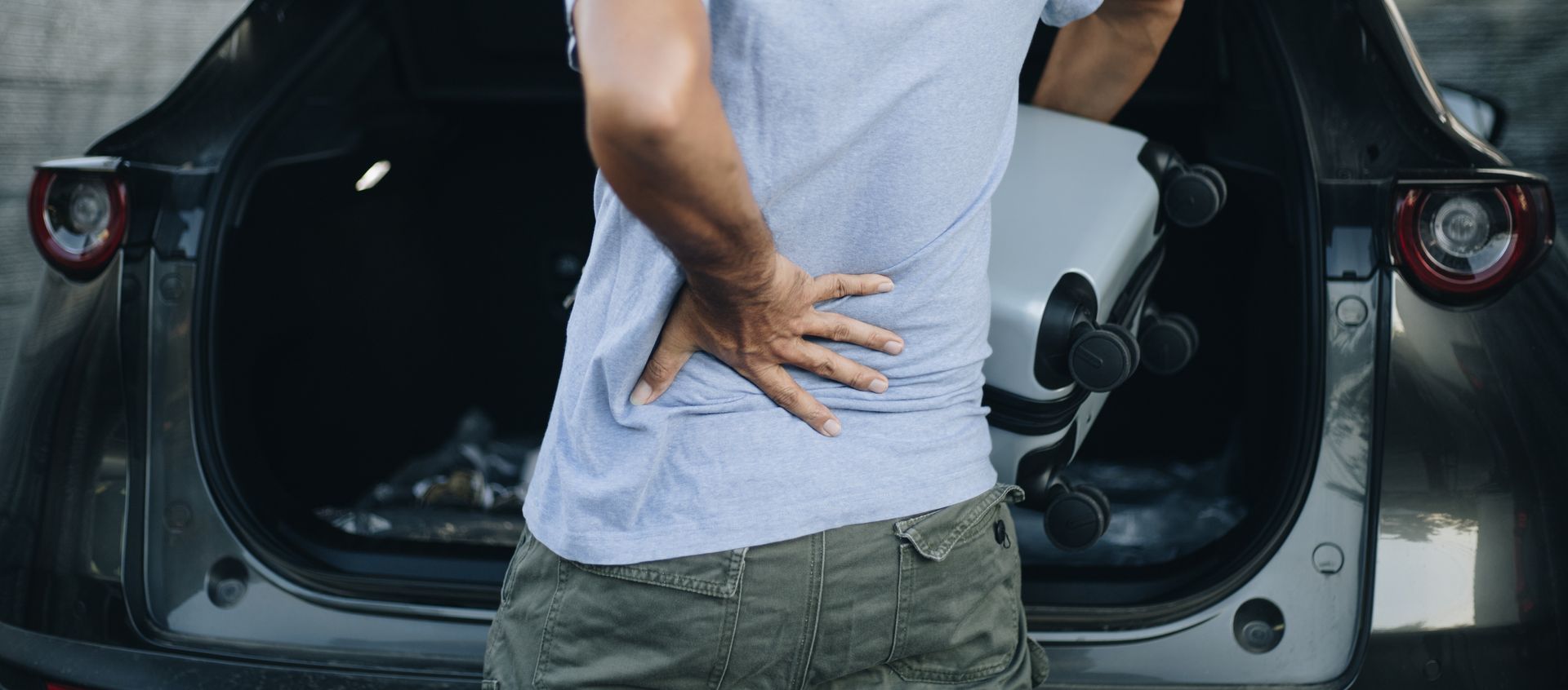 Person with hand on back, near car trunk, likely experiencing back pain.