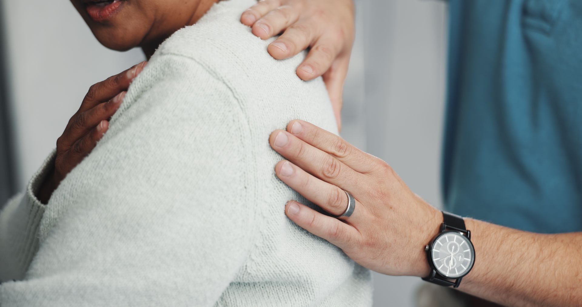 Person's shoulder being touched by another person's hand, suggesting care and support.