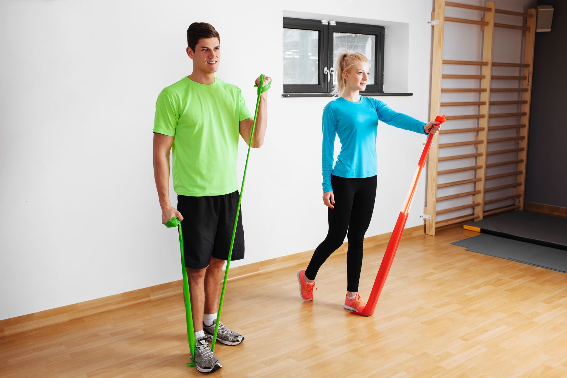 A man and a woman are doing exercises with resistance bands in a gym.