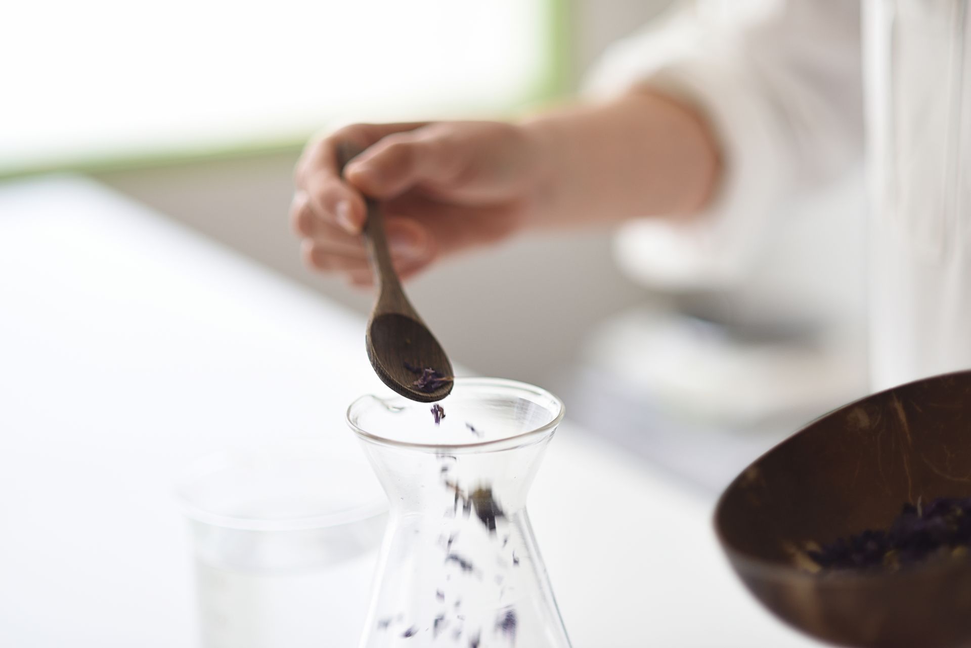 A person is pouring something into a beaker with a spoon.