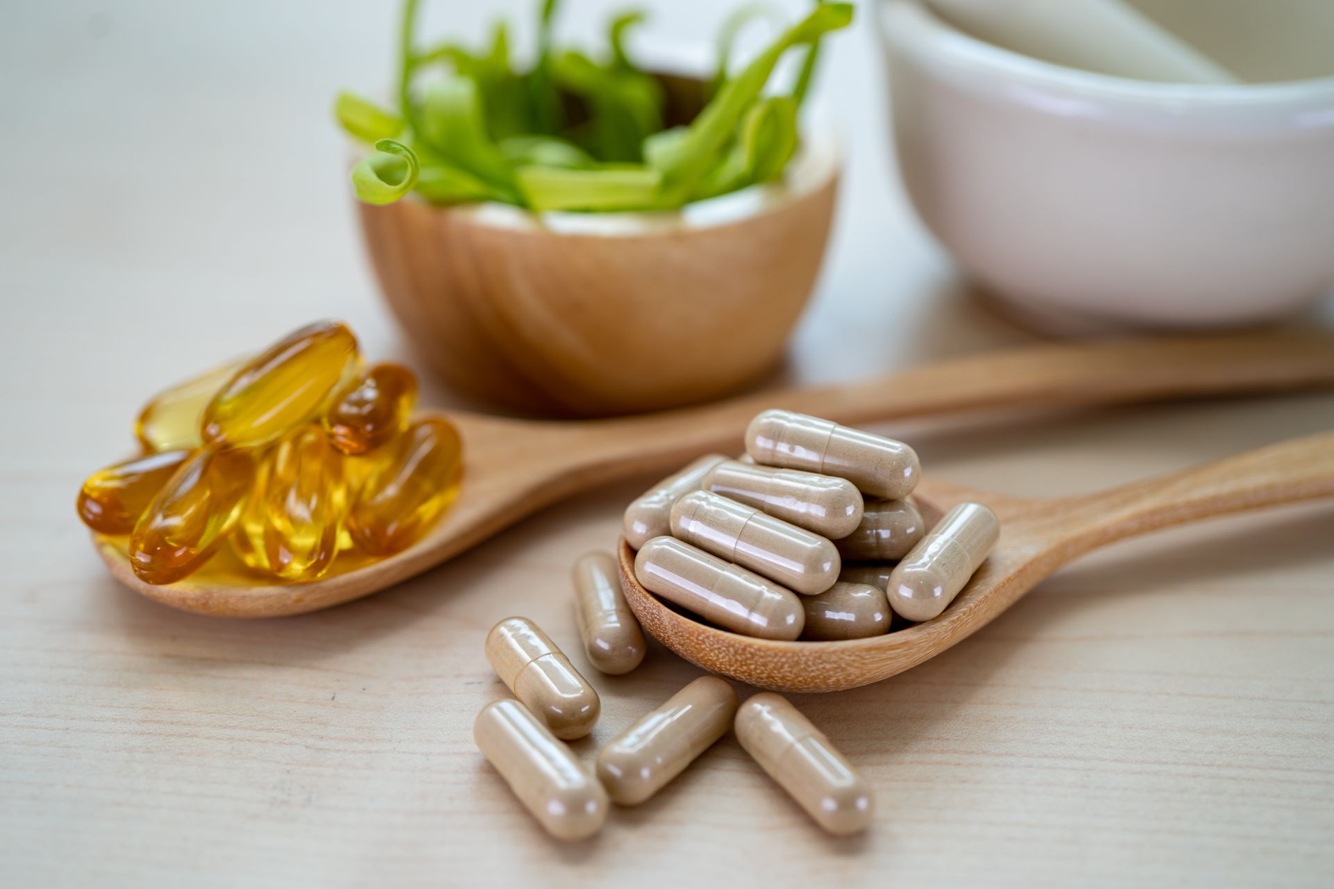 A wooden spoon filled with pills next to a bowl of pills and a mortar and pestle.