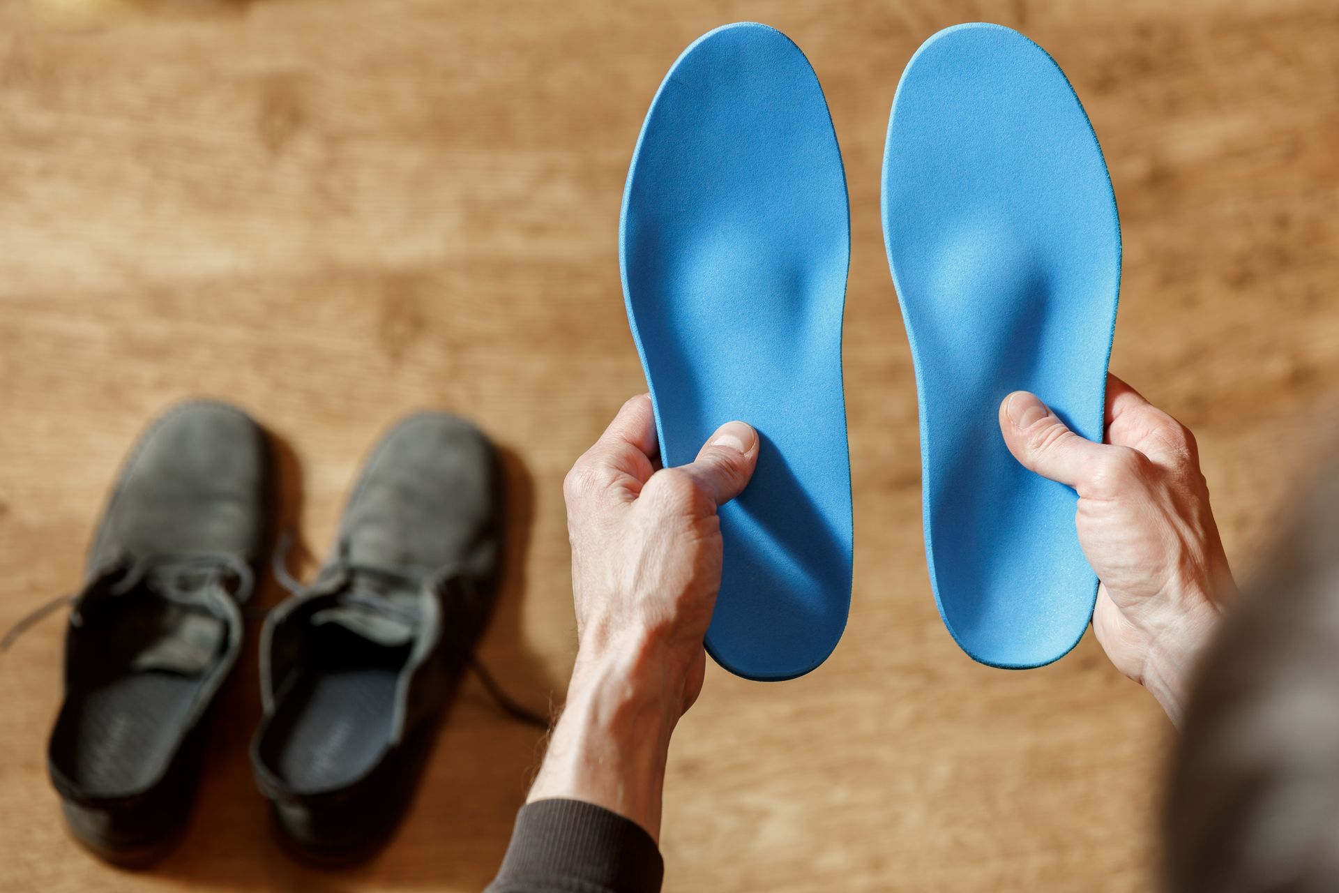 Hands holding blue insoles above a pair of black shoes on a wooden floor