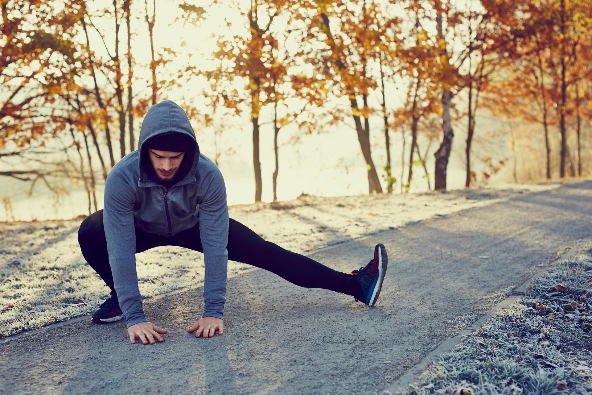 Person in a gray hoodie stretching on a gravel path among autumn trees.