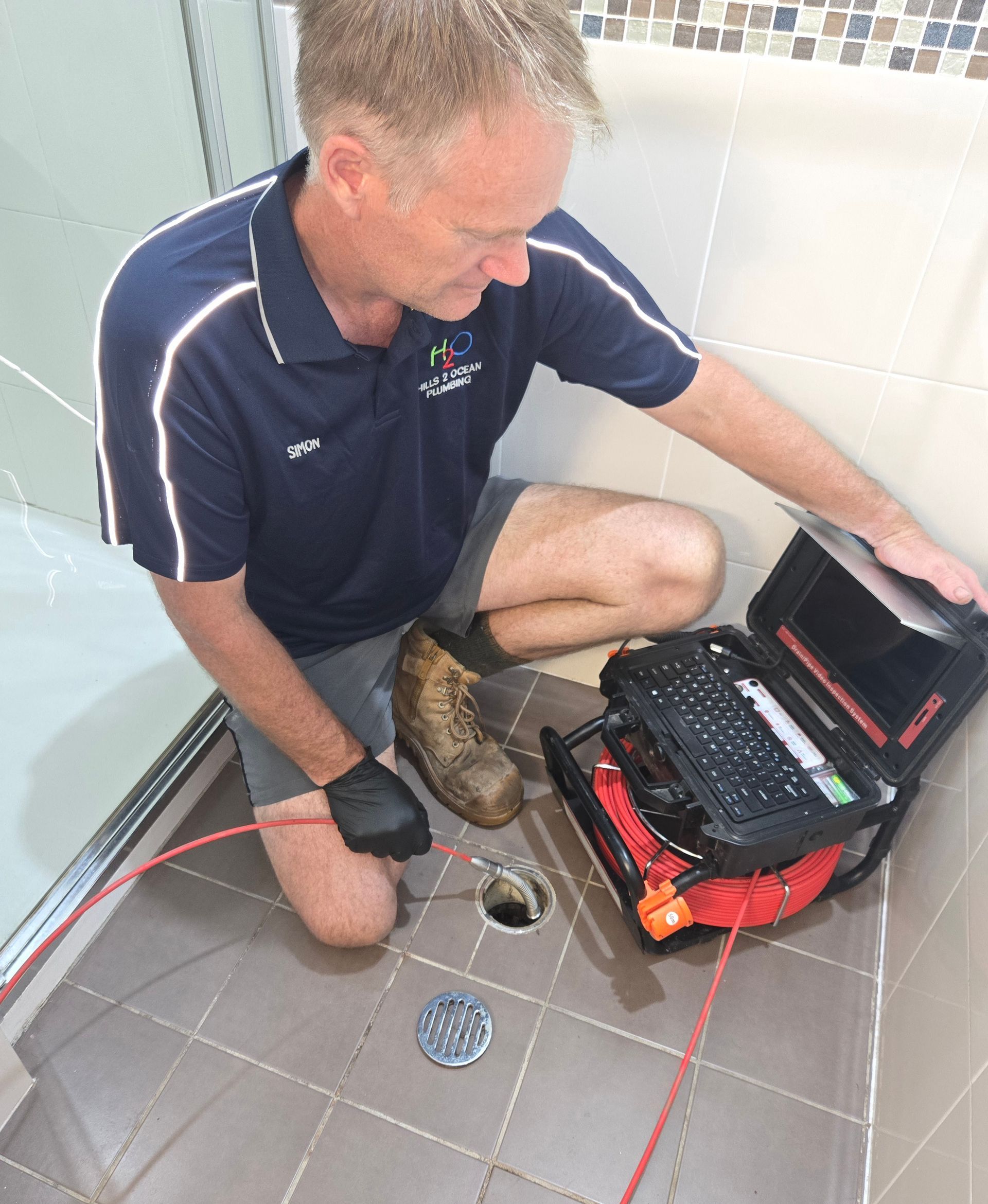 Man Inspecting a Shower Drain with A Camera, Wearing Work Clothes — Hills 2 Ocean Plumbing in Maclean, NSW
