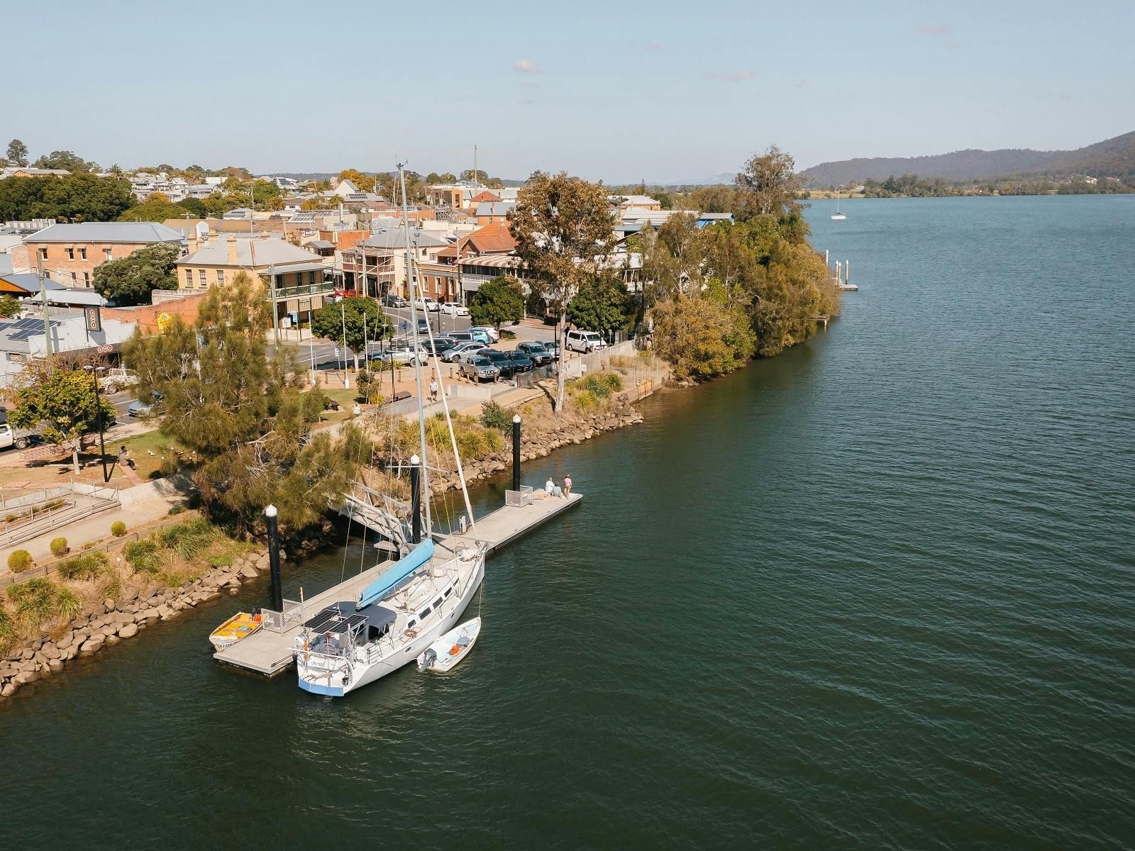 A Sailboat Docked at A Pier on A River Next to A Town — Hills 2 Ocean Plumbing in Maclean, NSW