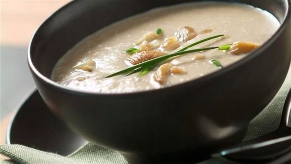 Sopa de champiñones en cuenco negro, adornada con cebollino y champiñones.