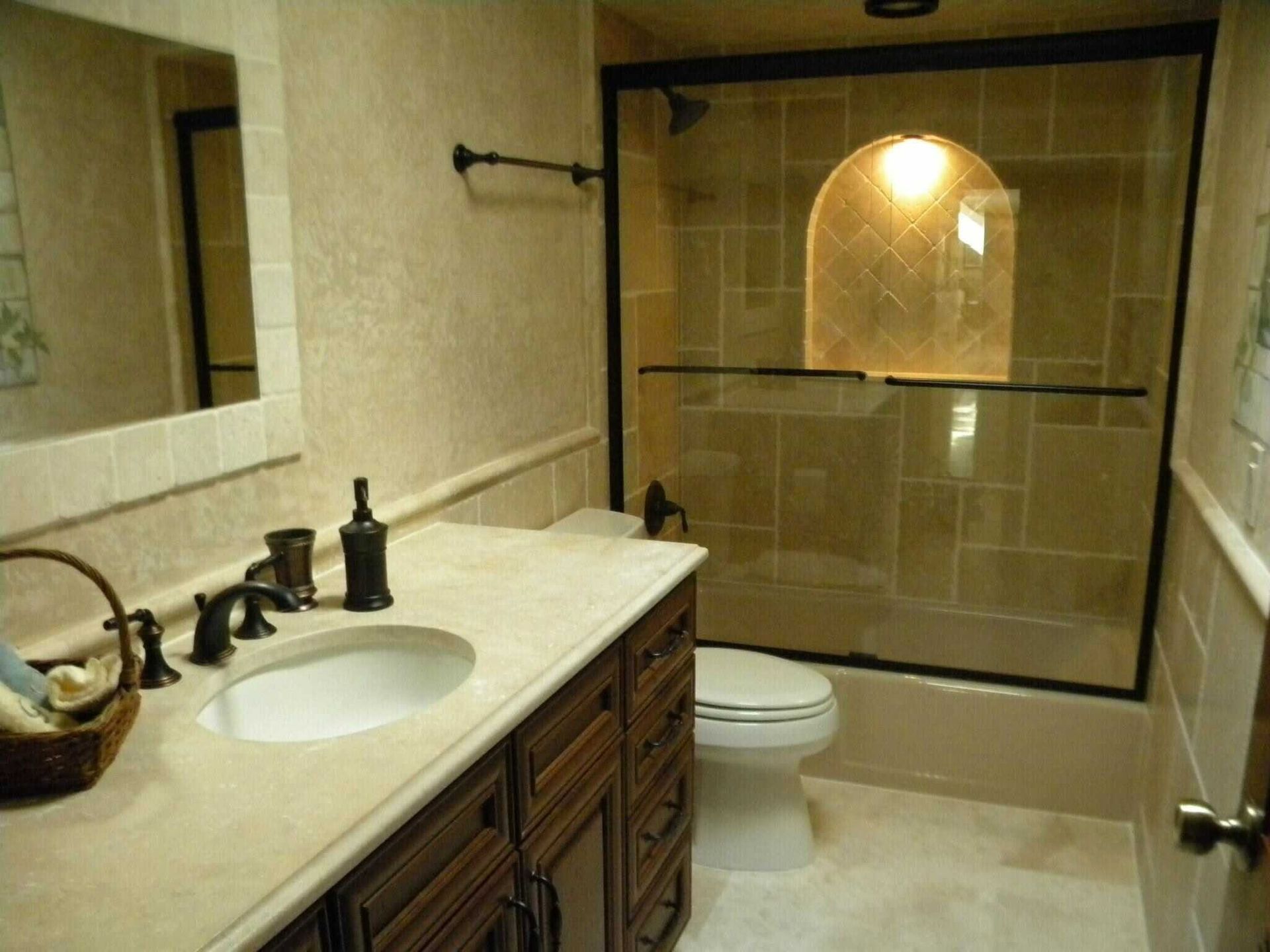 Bathroom with vanity sink, toilet, and glass-enclosed shower in beige tile.