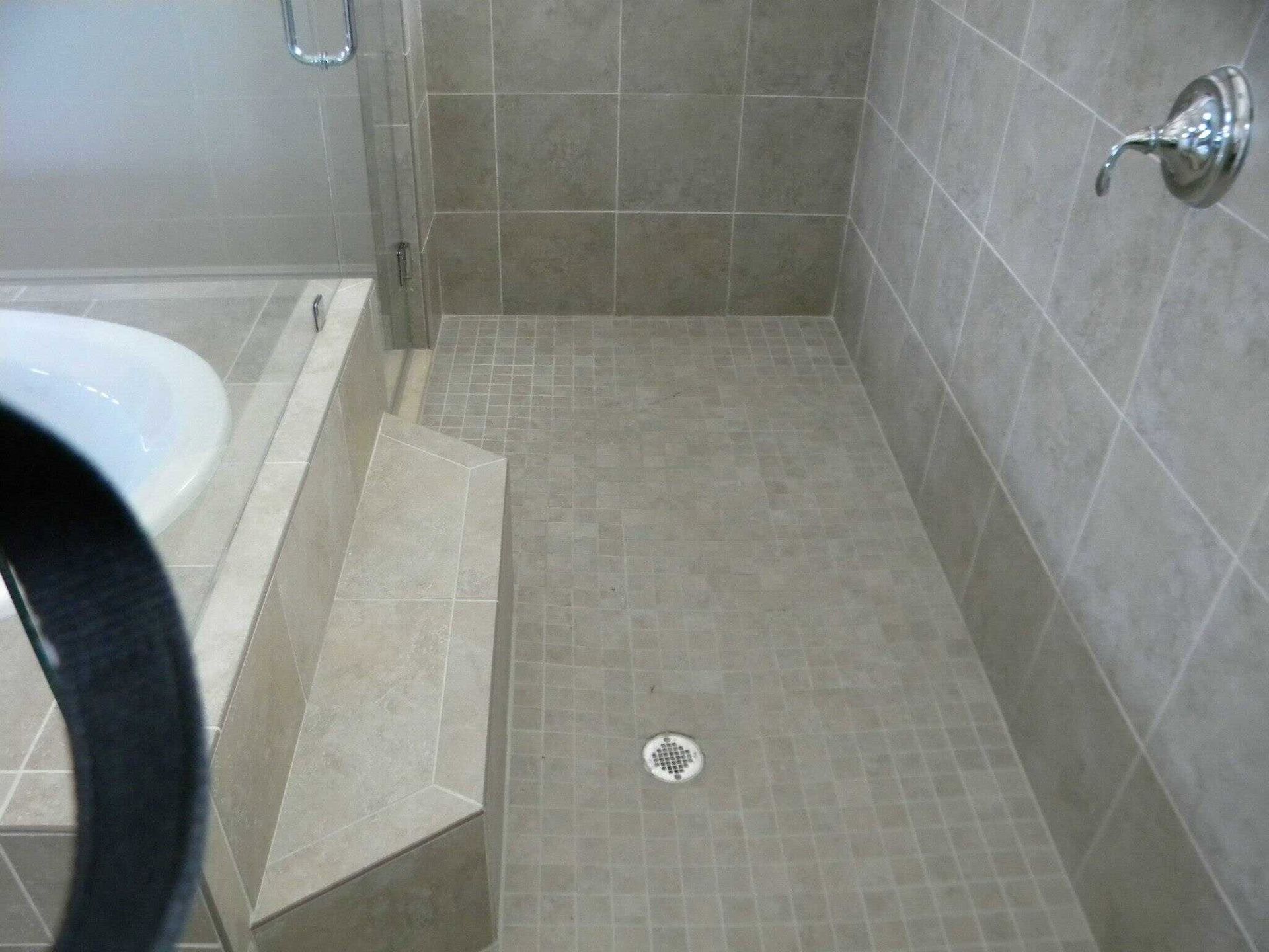Bathroom with tiled walk-in shower, sloped bench, and floor drain.