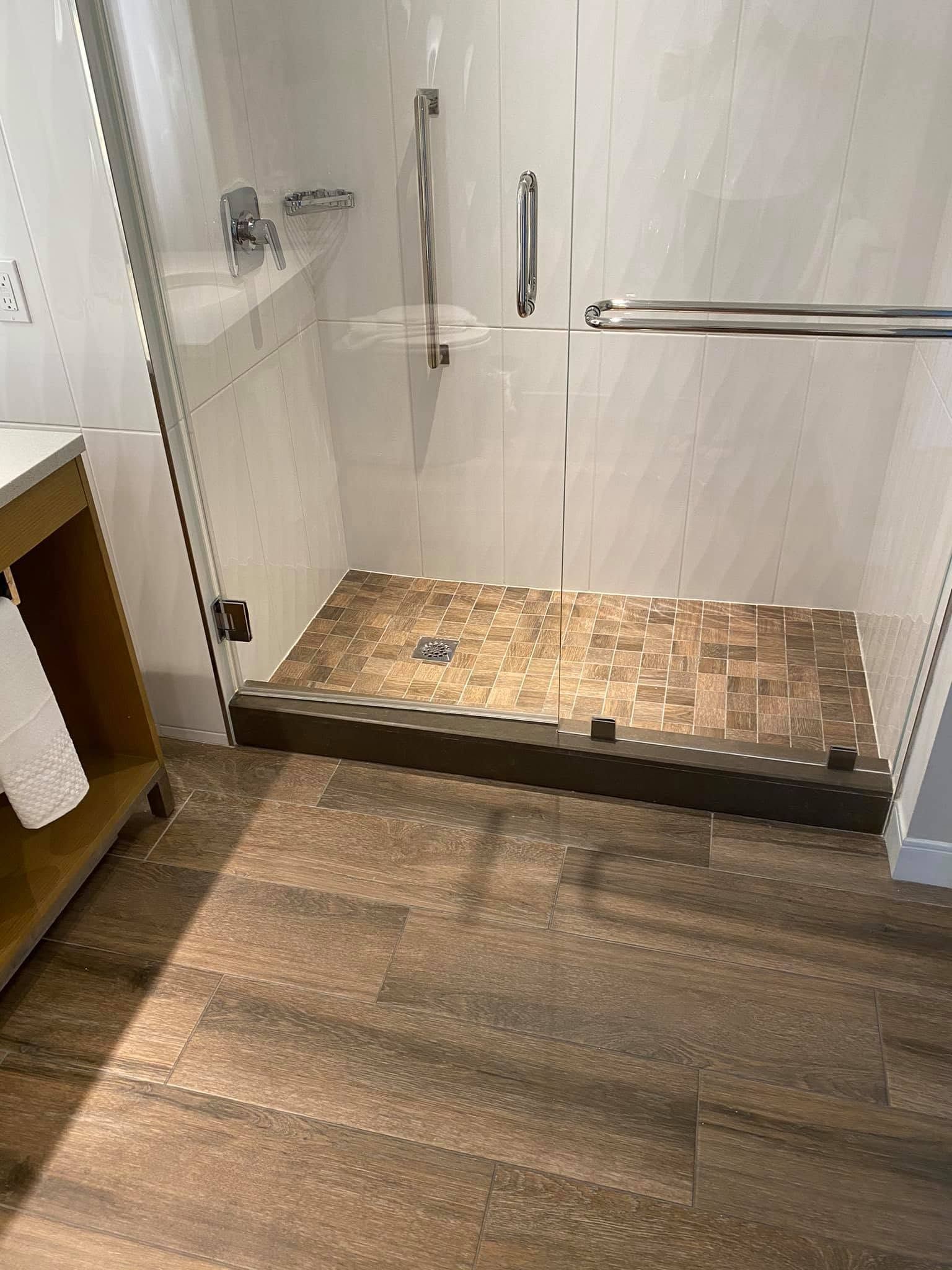 Walk-in shower with white tile walls, glass door, and wood-look flooring in a bathroom