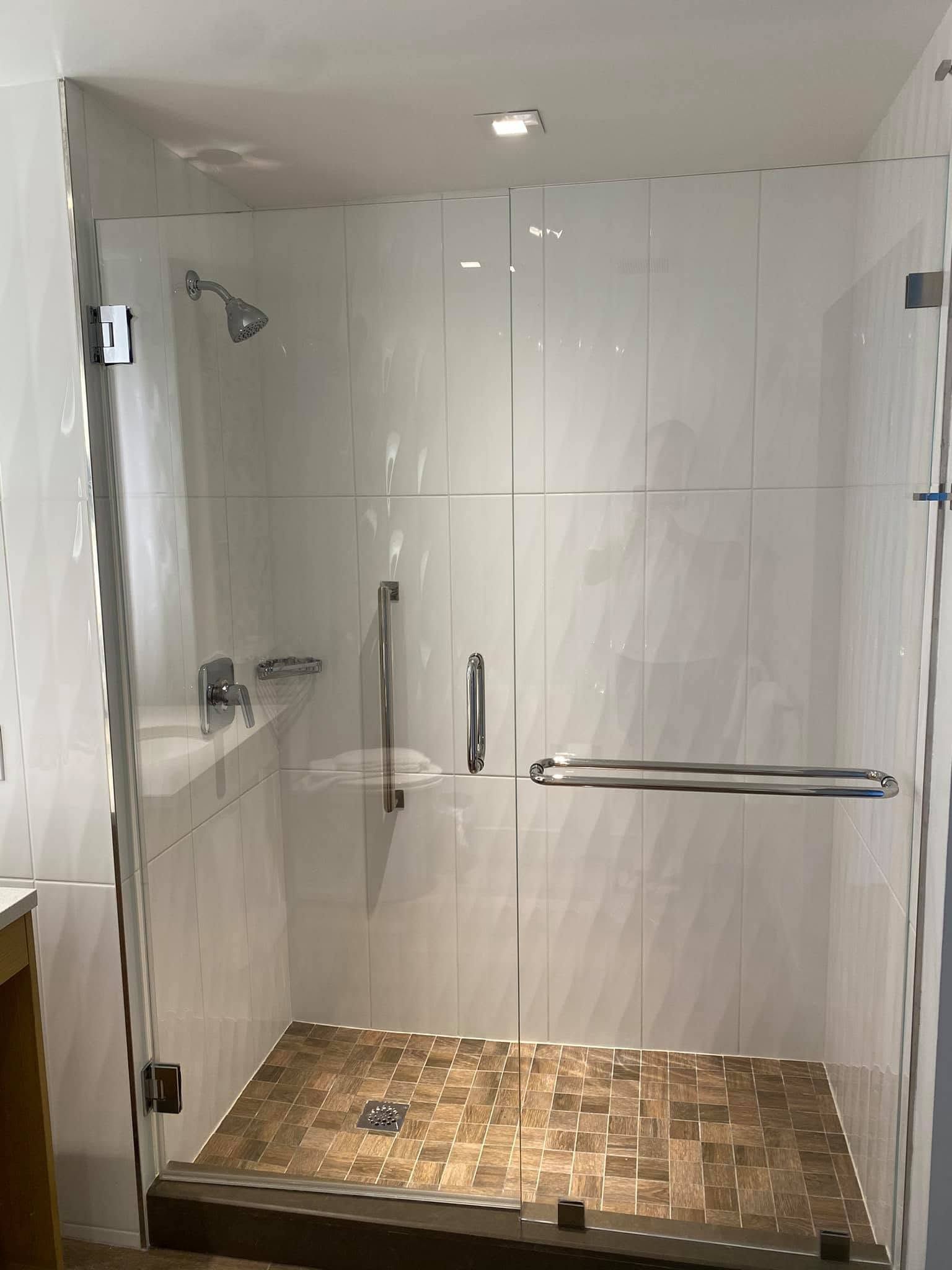 Accessible bathroom with glass shower enclosure, grab bars, and tiled floor.