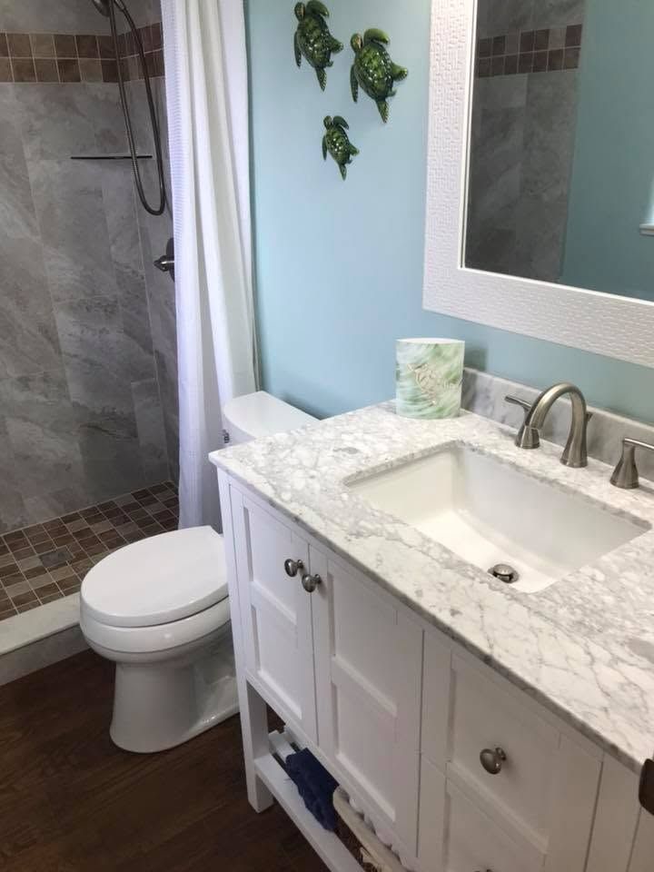 Small bathroom with white vanity, marble countertop, toilet, and tiled shower.