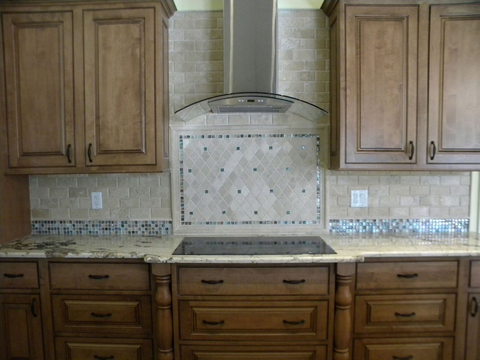 Kitchen with wooden cabinets, mosaic tile backsplash, and stainless steel range hood over a cooktop.