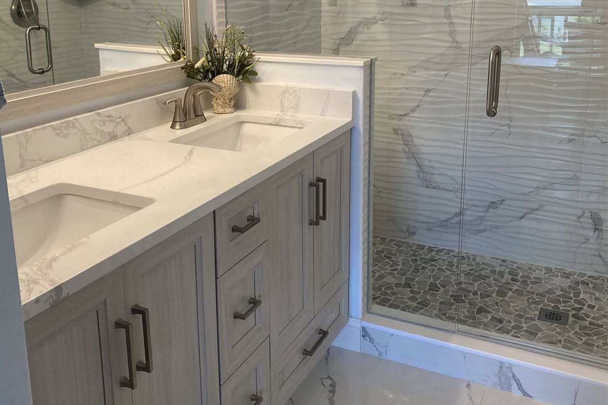 Modern bathroom vanity with white marble countertop, gray cabinets, and glass shower in the background