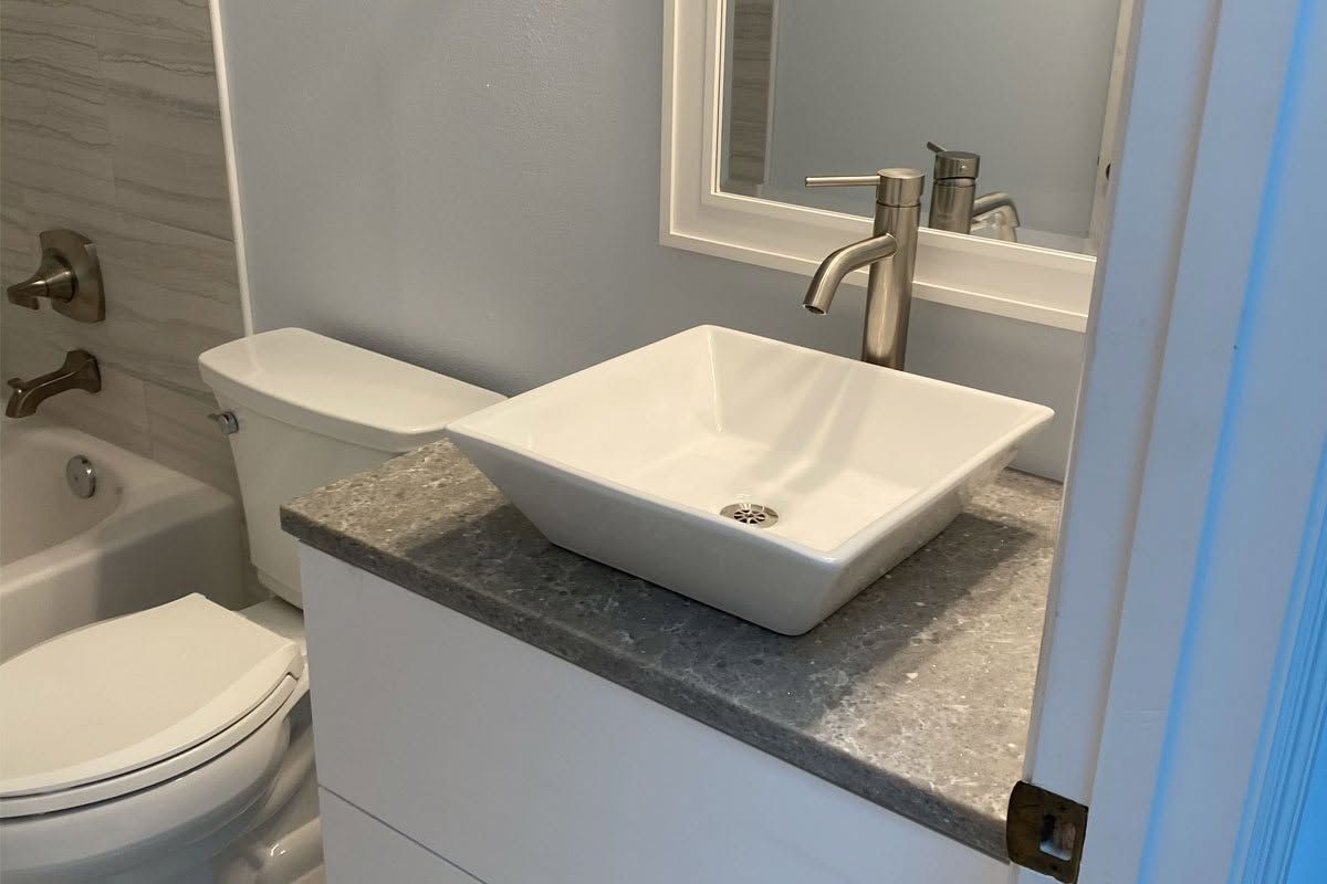Small bathroom with toilet, bathtub, and a white vessel sink on a gray countertop.