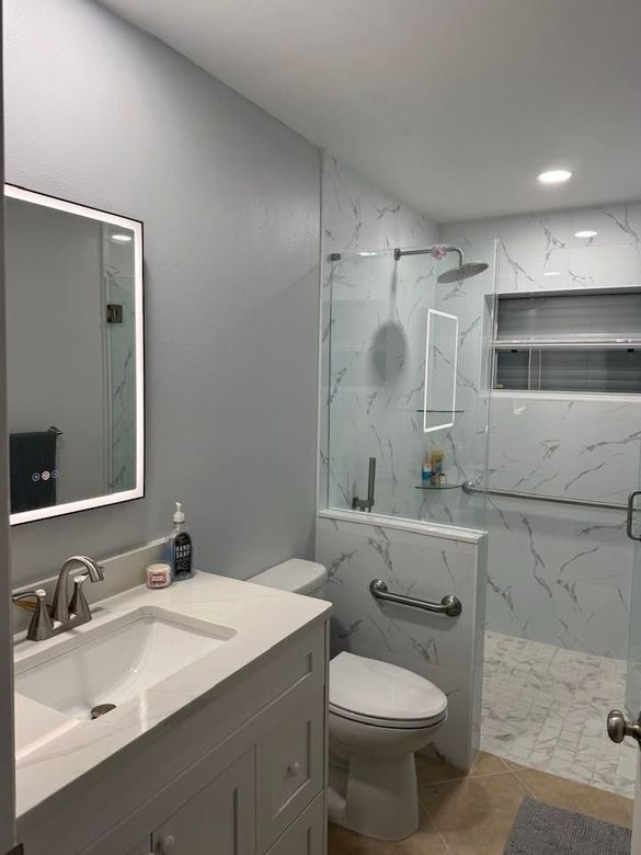 Small gray bathroom with white vanity, toilet, glass shower, and tiled walls