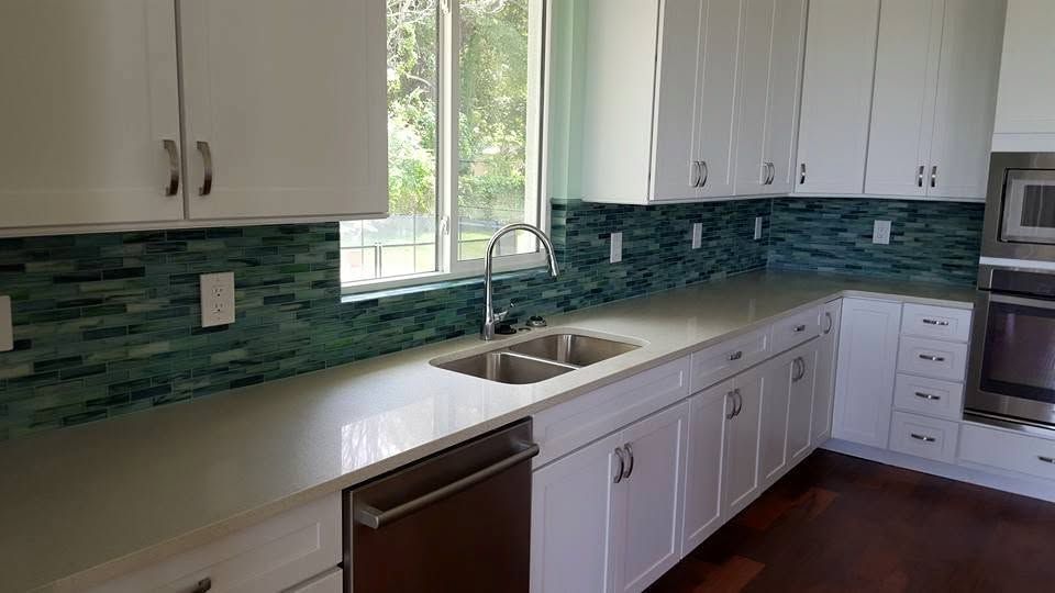 Bright kitchen with white cabinets, teal backsplash, long counter, sink, and window.