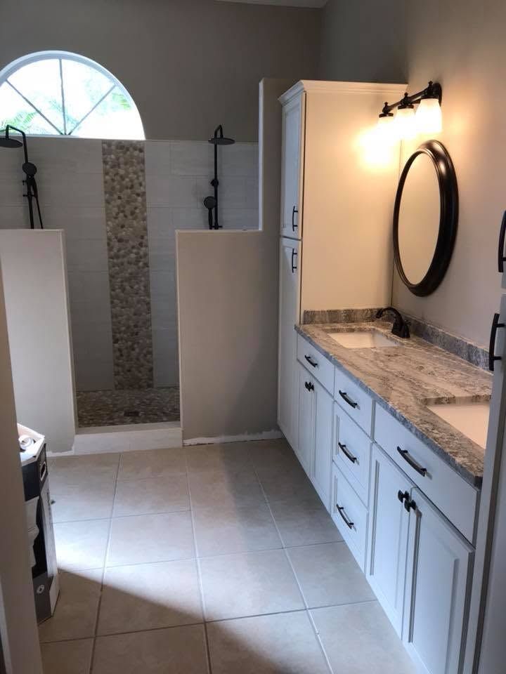 Bright bathroom with walk-in shower, white vanity, marble countertop, and arched window.