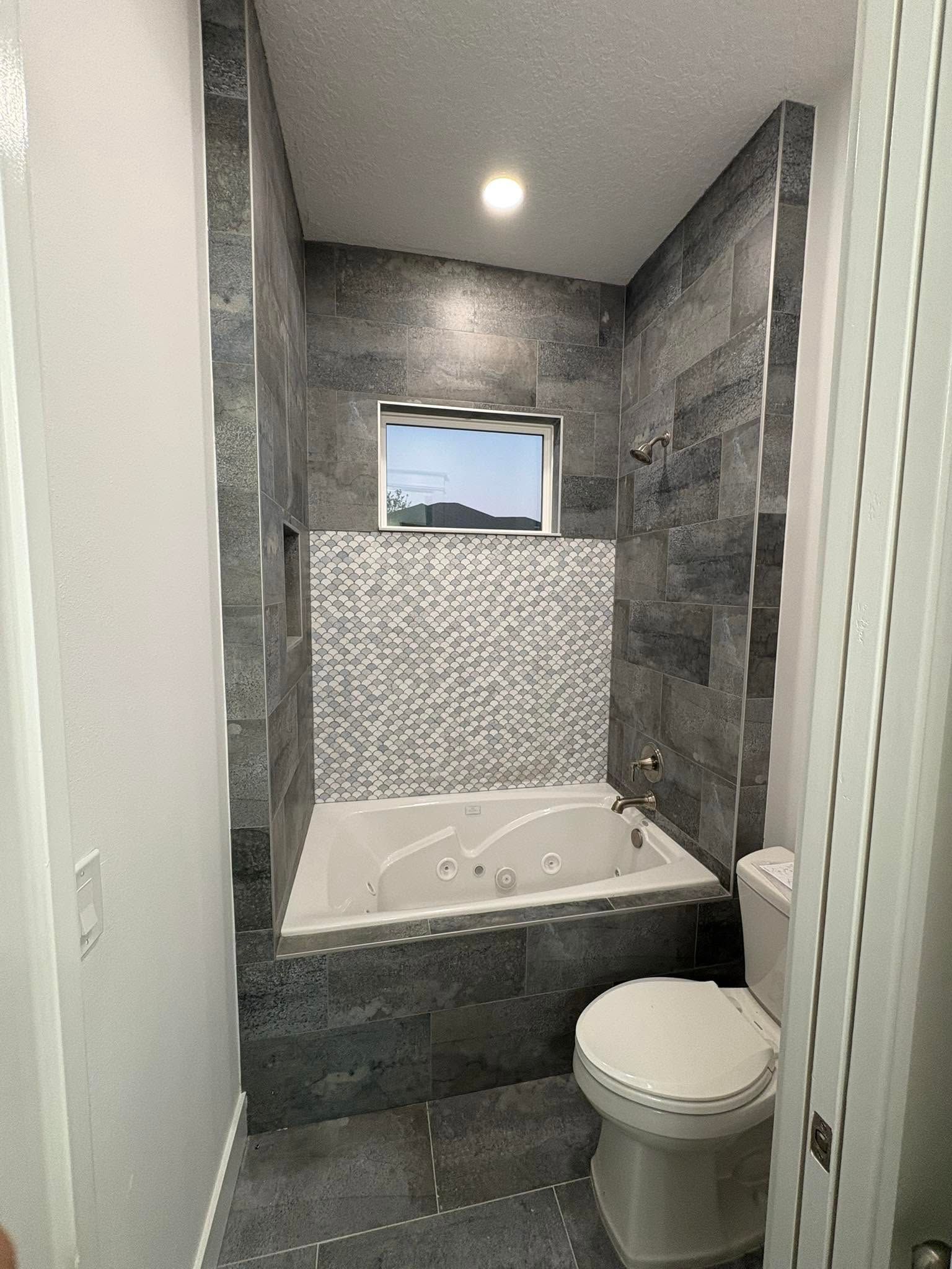 Small modern bathroom with a bathtub-shower combo, tiled walls, window, and toilet.