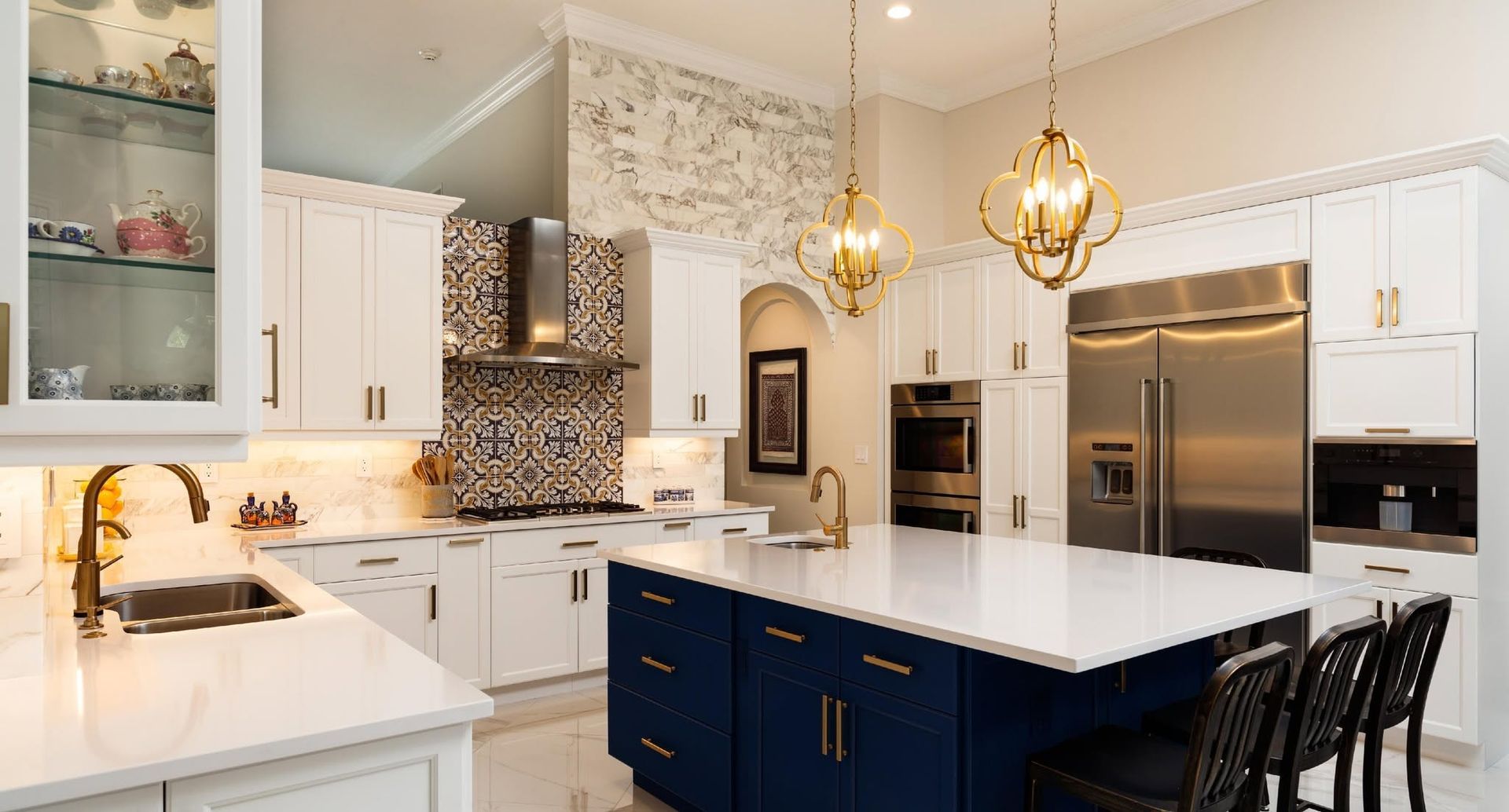 Bright modern kitchen with white cabinets, navy island, stainless steel appliances, and gold pendant lights