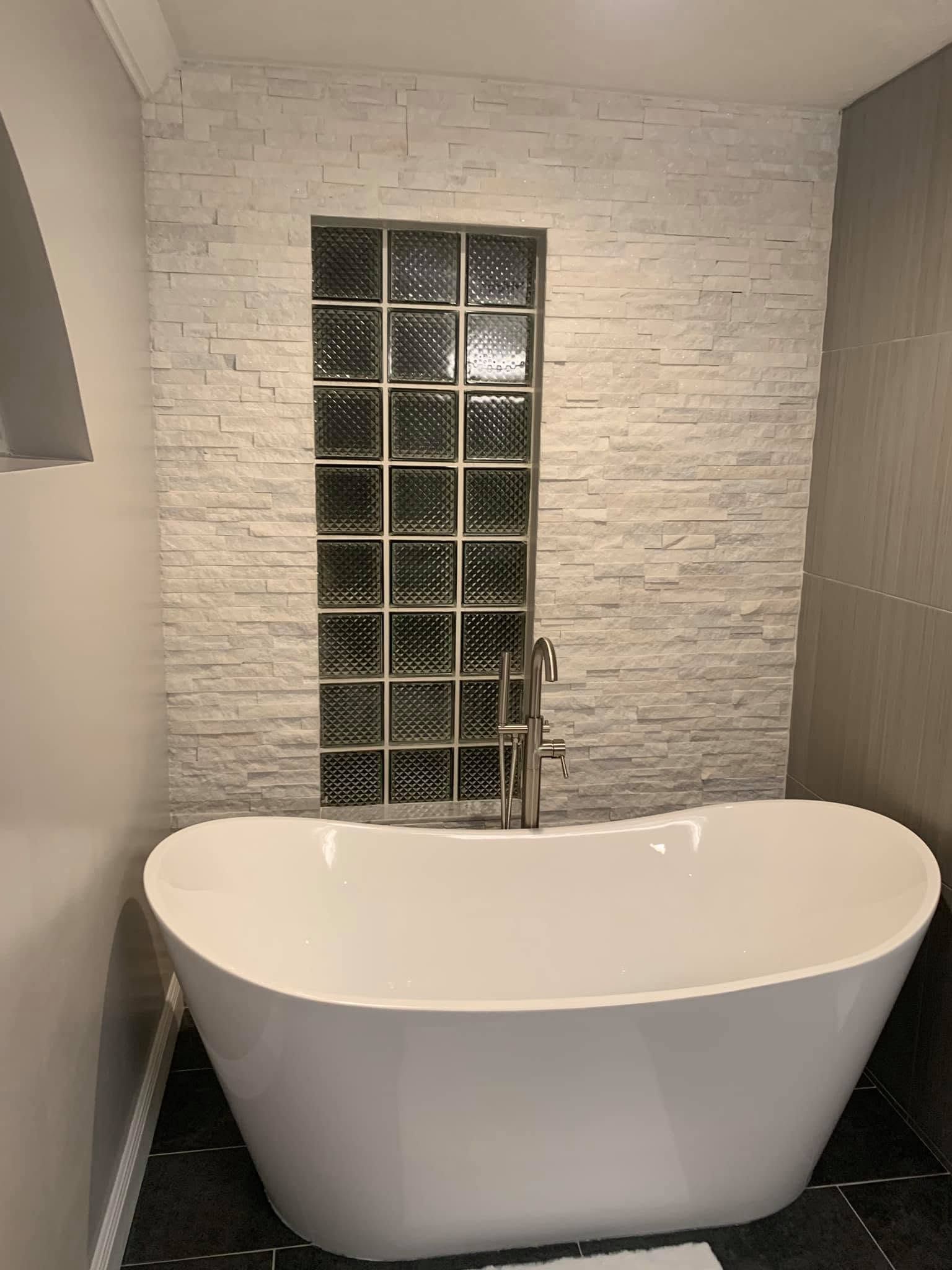 Modern bathroom with a white freestanding tub in front of a glass-block window and white brick wall