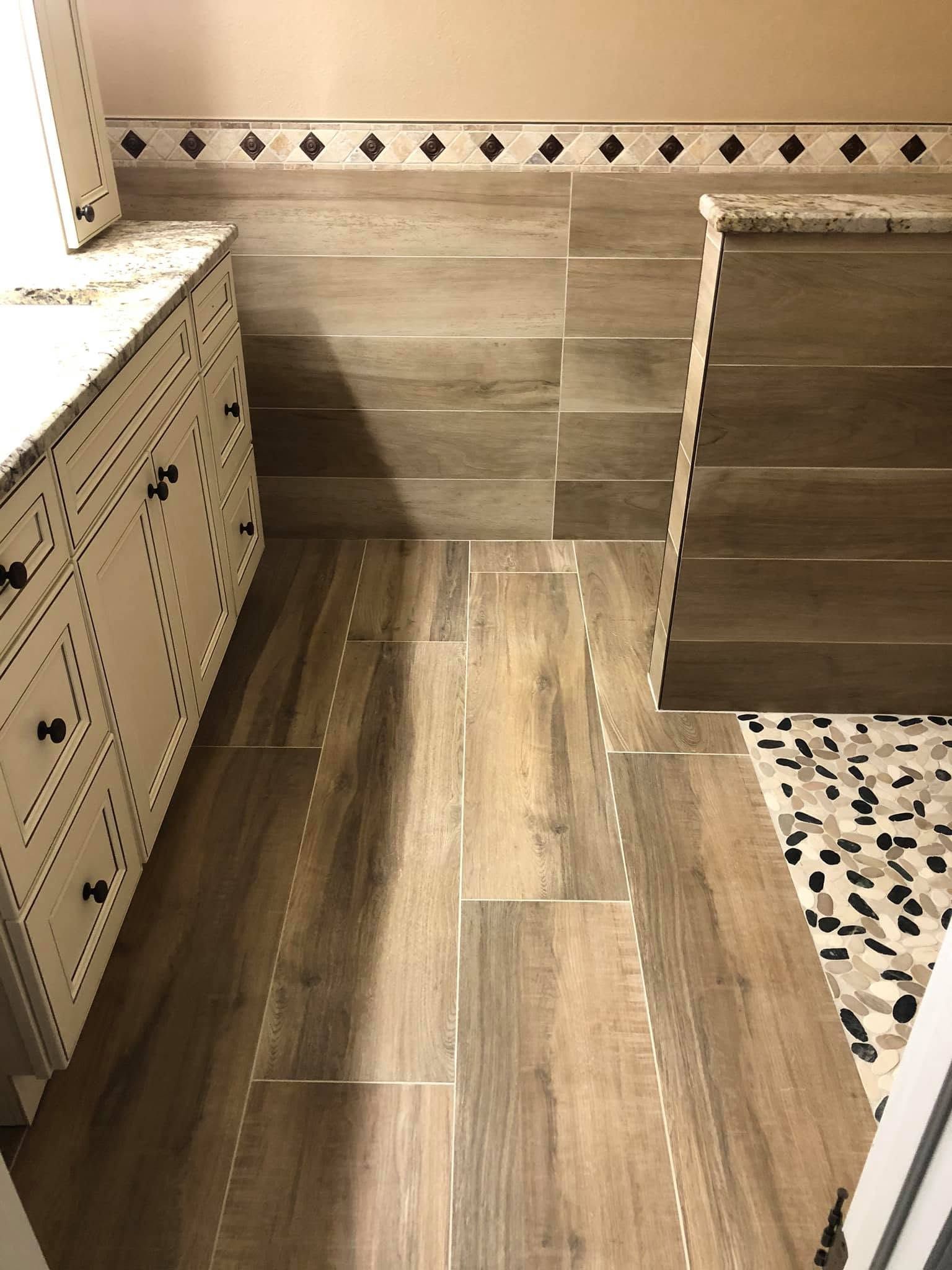 Small bathroom with wood-look floor, patterned tile walls, and a partially visible shower curb.