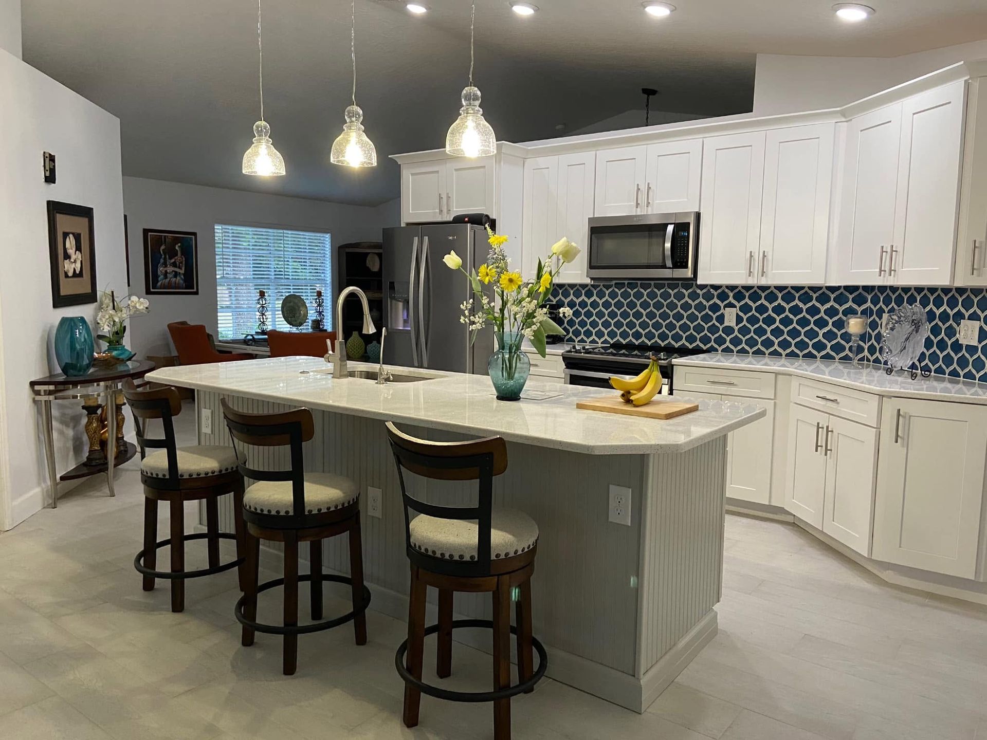 Bright kitchen with white cabinets, blue tile backsplash, island, bar stools, and hanging pendant lights.