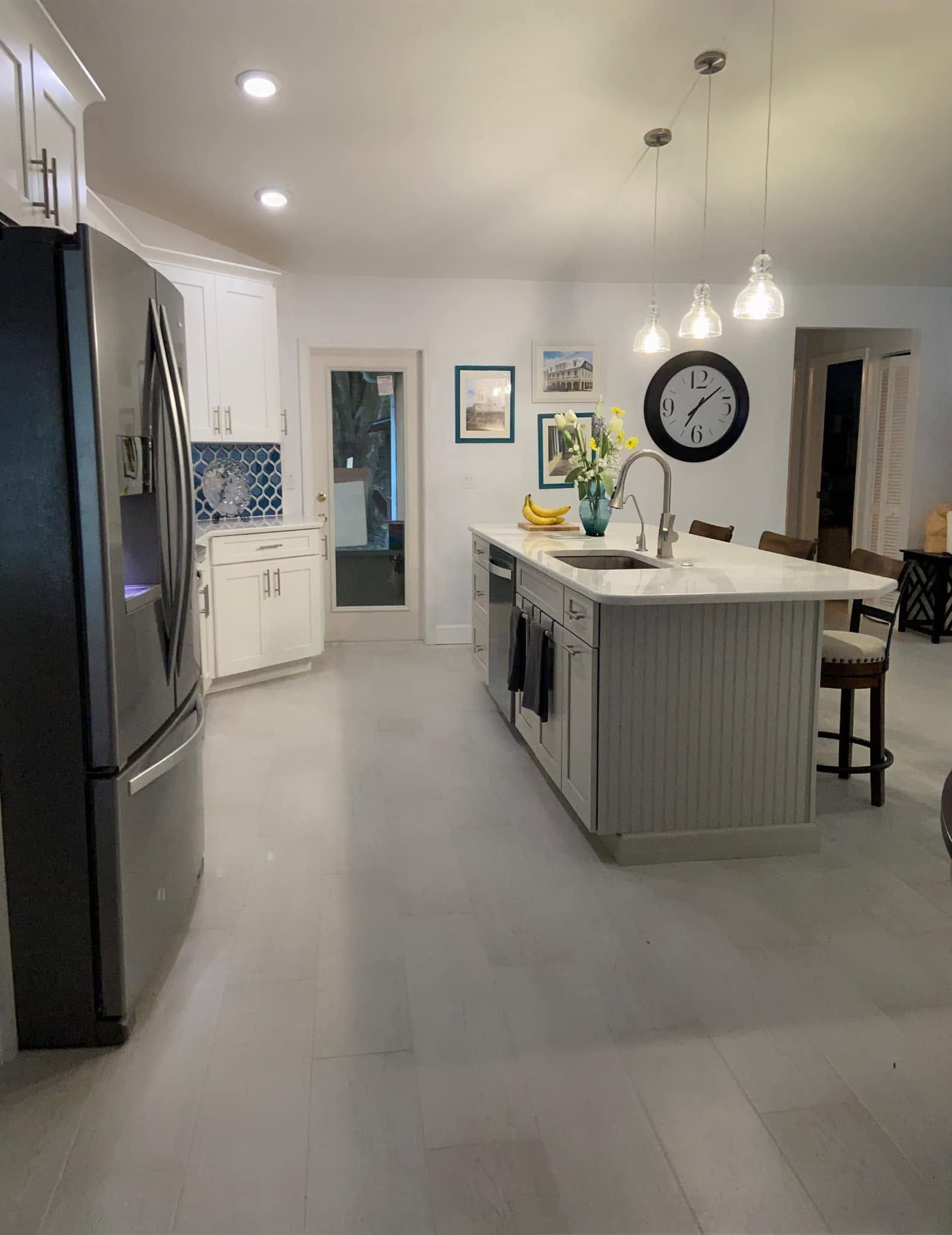 Modern kitchen with gray island, large wall clock, stainless fridge, and pendant lights