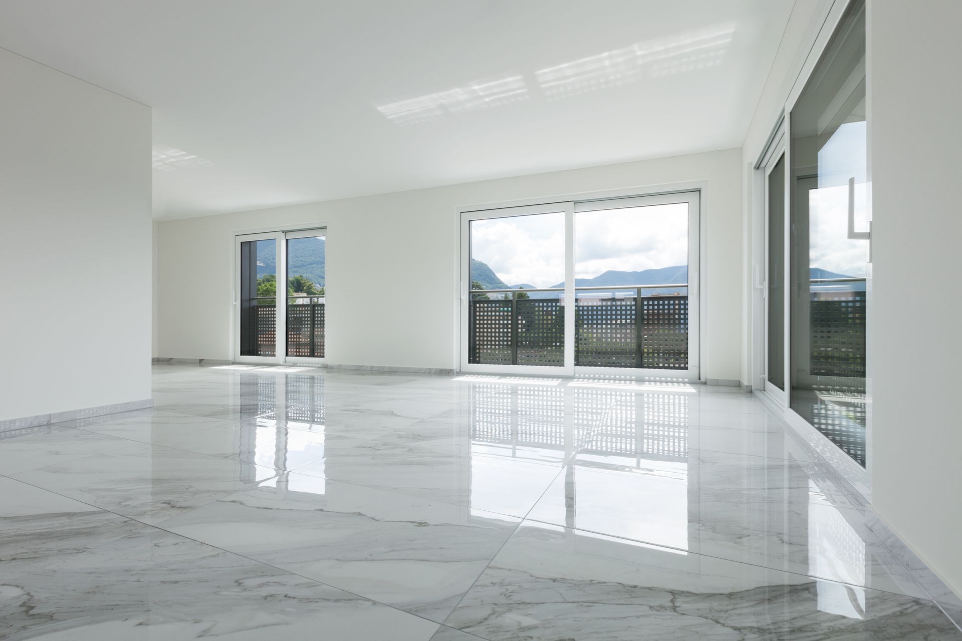 Bright empty room with glossy marble floor and large windows overlooking a balcony and mountains. Bright empty room with glossy marble floor and large windows overlooking a balcony and mountains.