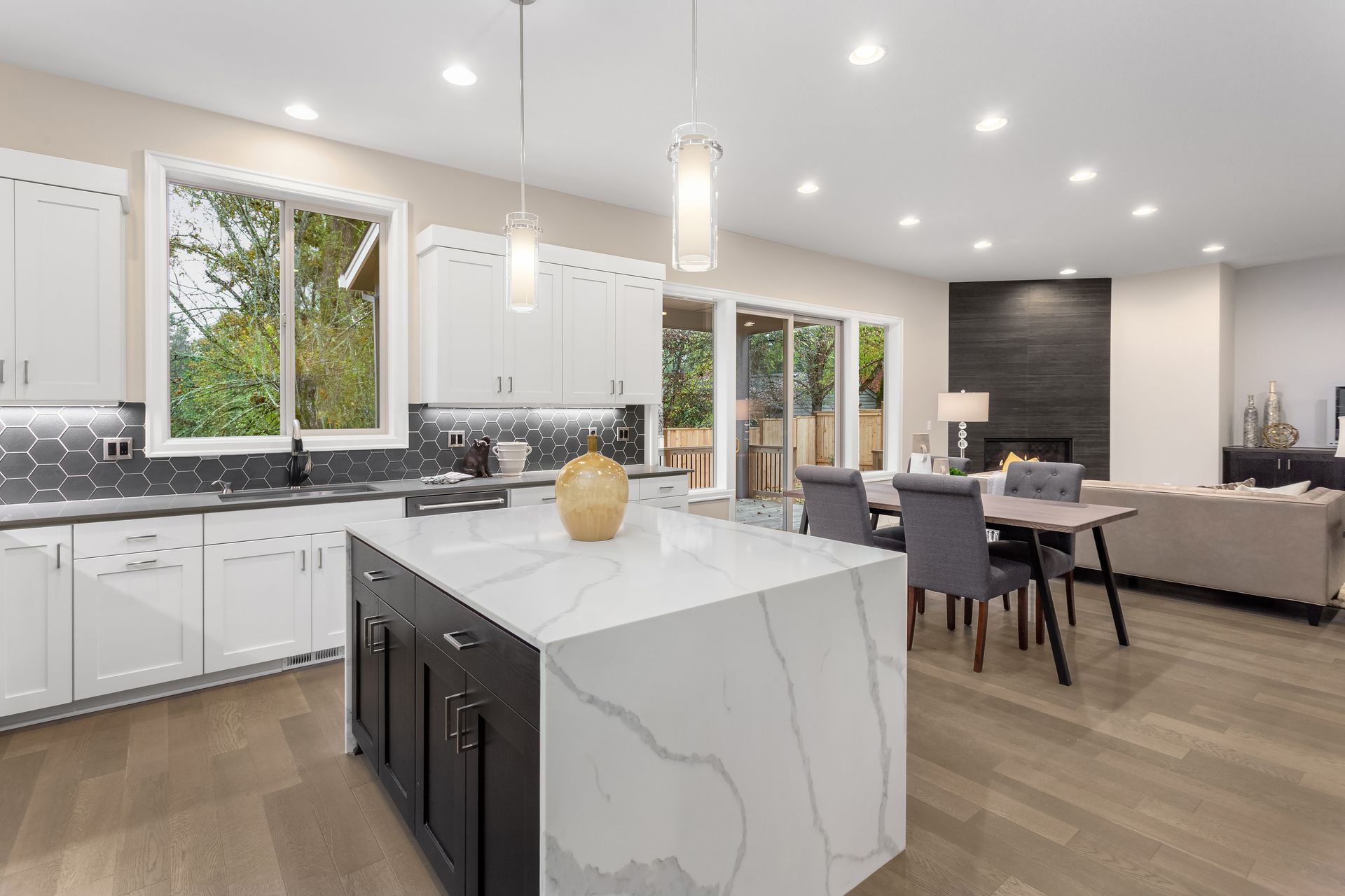 Bright modern kitchen and dining area with white cabinets, marble island, and gray sofa in open floor plan
