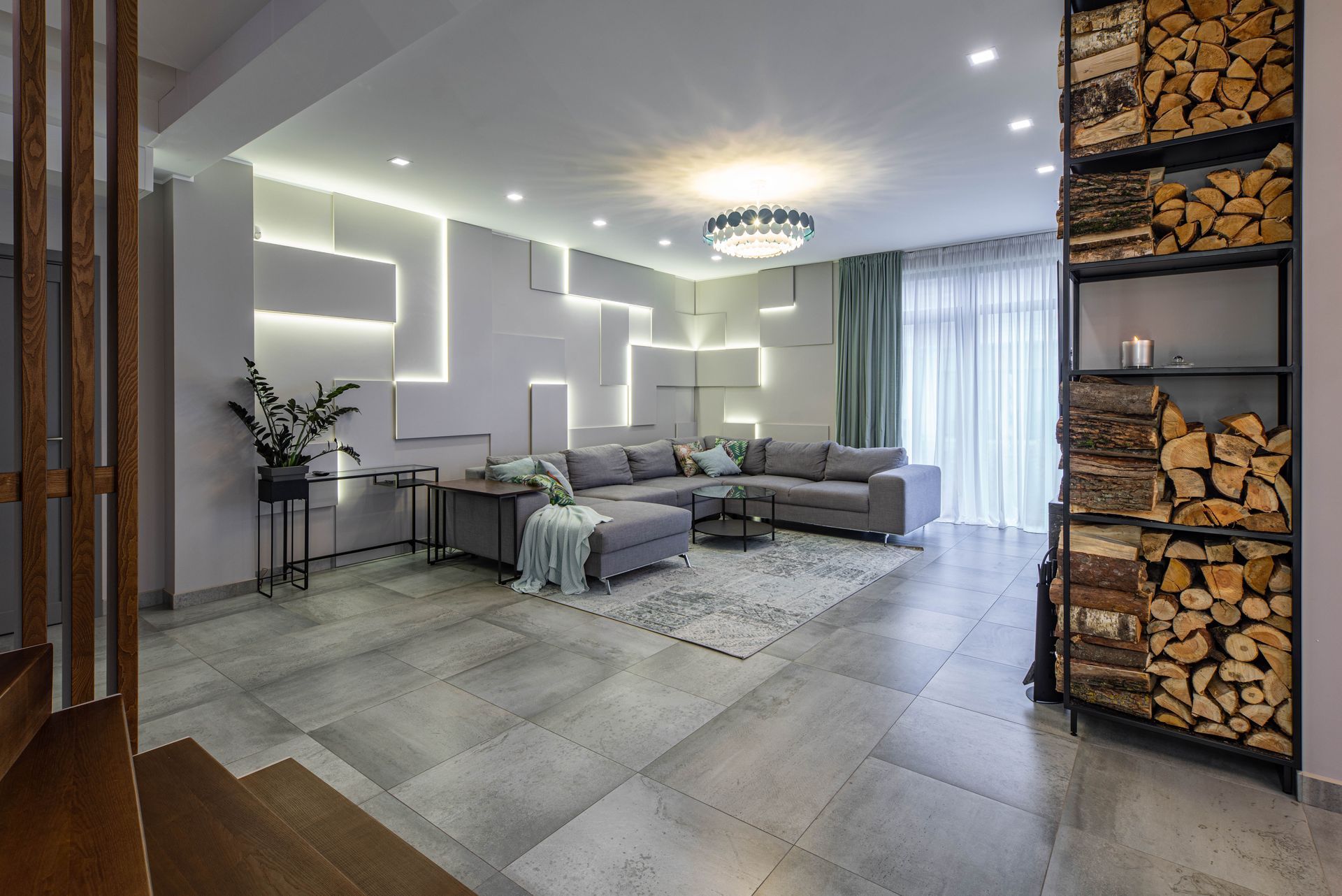 Modern living room with gray sectional sofa, geometric wall lights, and a stacked firewood display Modern living room with gray sectional sofa, geometric wall lights, and a stacked firewood display