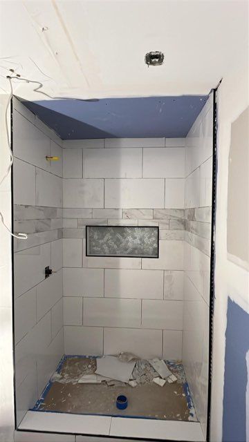 Shower stall under construction, tiled walls and blue ceiling, unfinished floor, wiring visible.