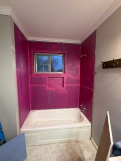 Bathroom renovation in progress, walls painted bright pink around a white bathtub and window.