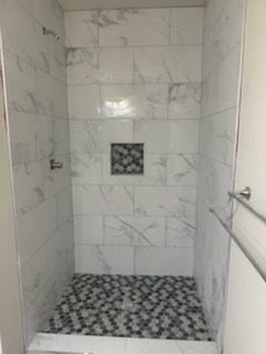 White marble-tiled shower with a patterned mosaic floor. A dark tiled inset is centered on the back wall.