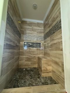 Bathroom with beige and dark stone tile. Includes a built-in bench and recessed shelf.