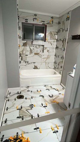 Bathroom under construction, white marble tiles on walls and floor, tub and window visible.