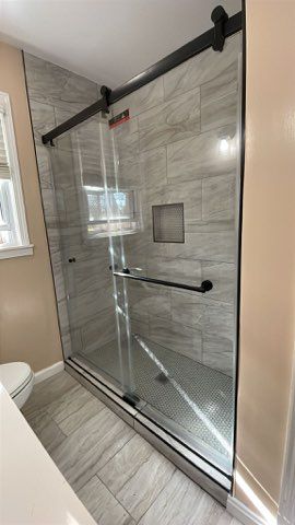 Modern shower enclosure with sliding glass door and black hardware.