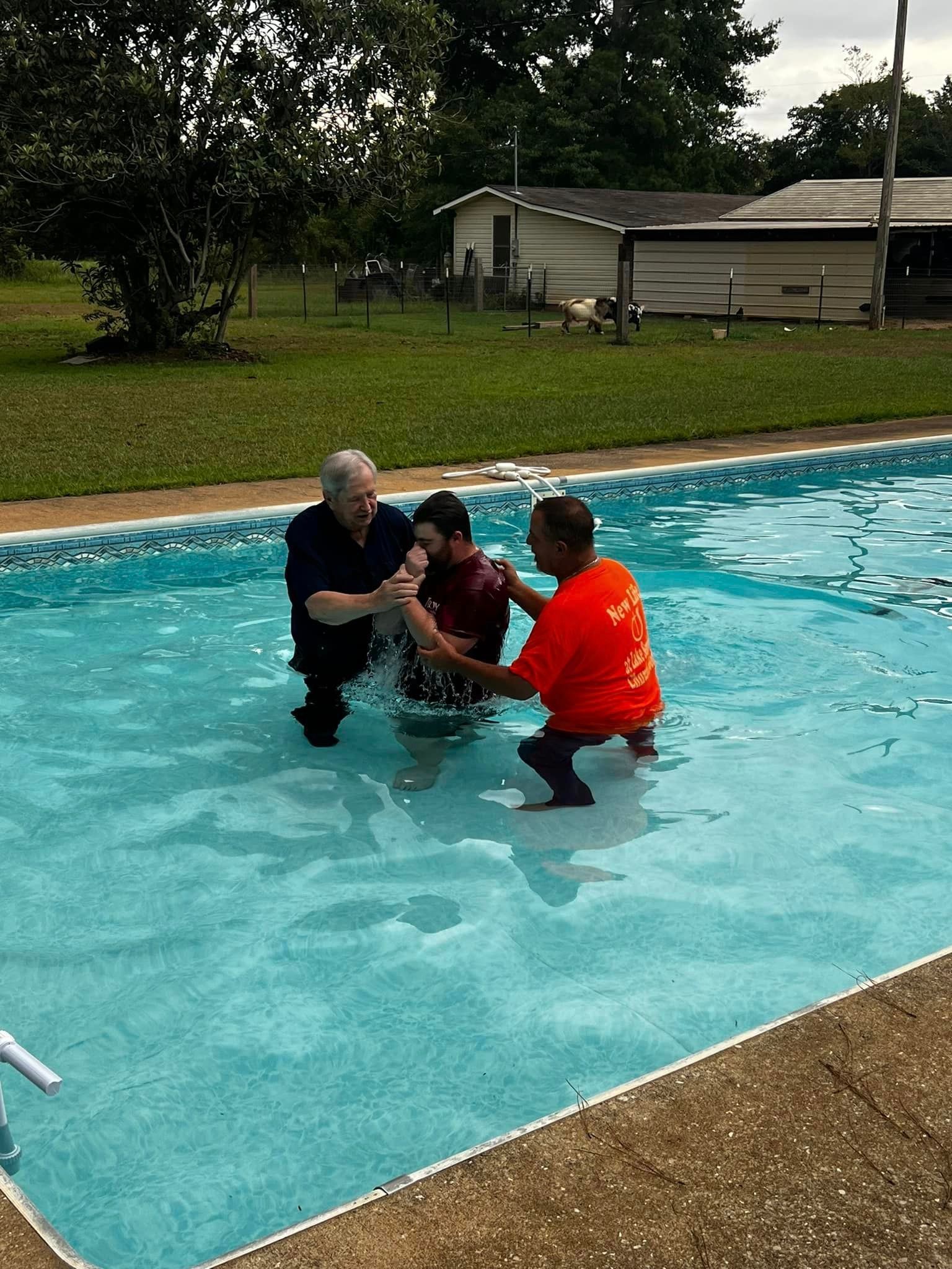 A man in an orange shirt is baptizing a child in a pool