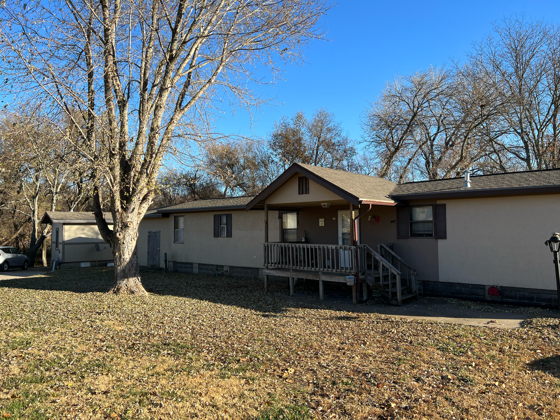 A mobile home with a porch and a tree in front of it.
