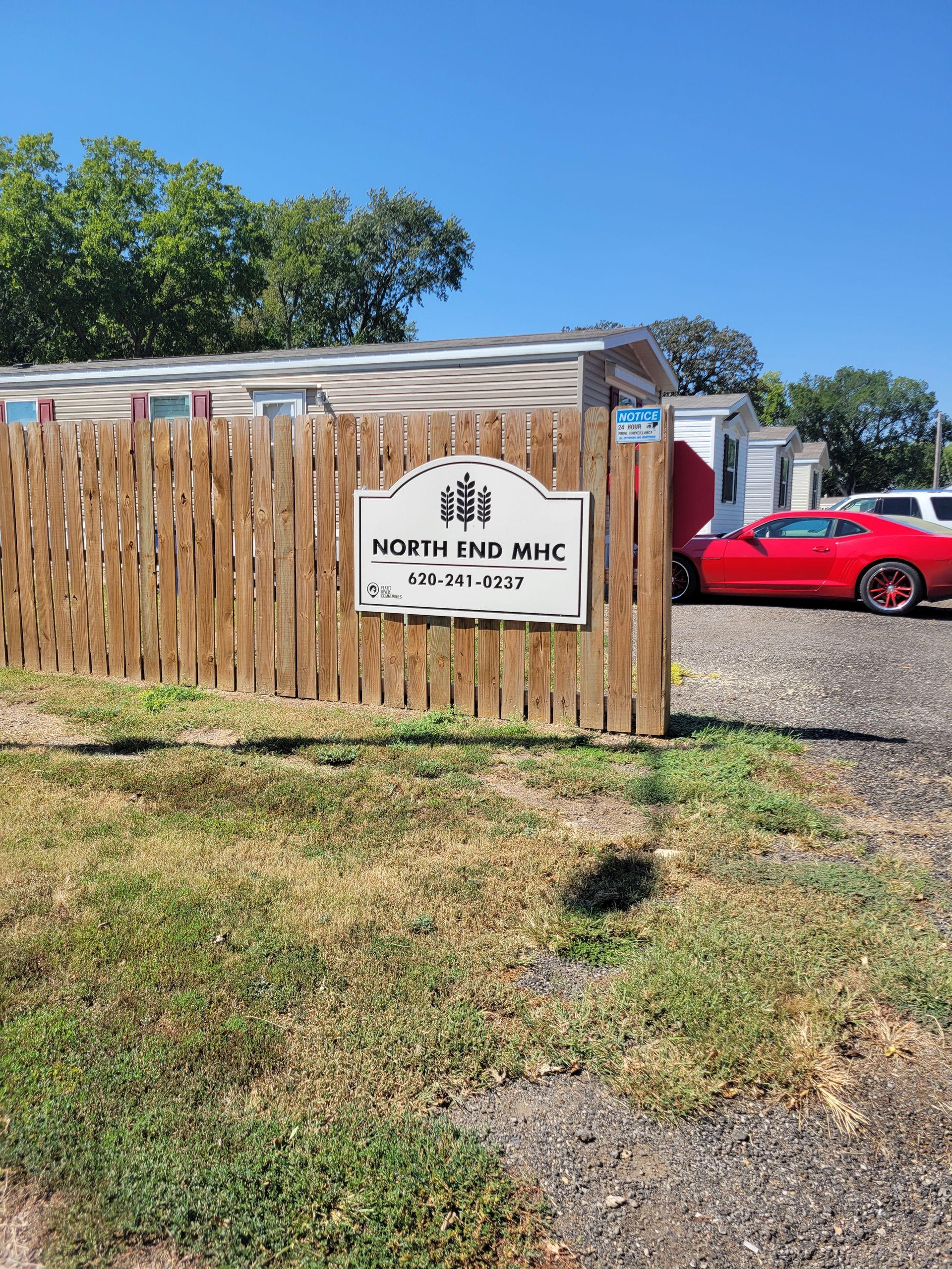 A red car is parked in front of a wooden fence.