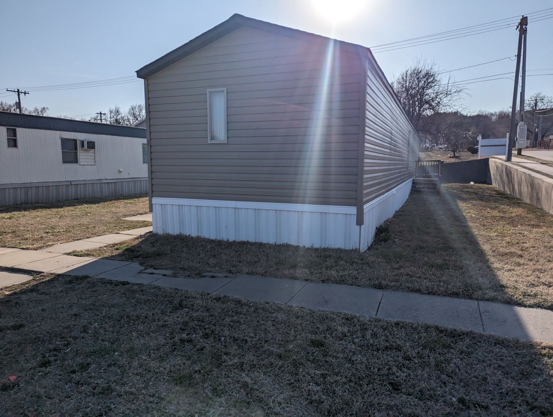 A mobile home is sitting in the middle of a grassy field next to a sidewalk.