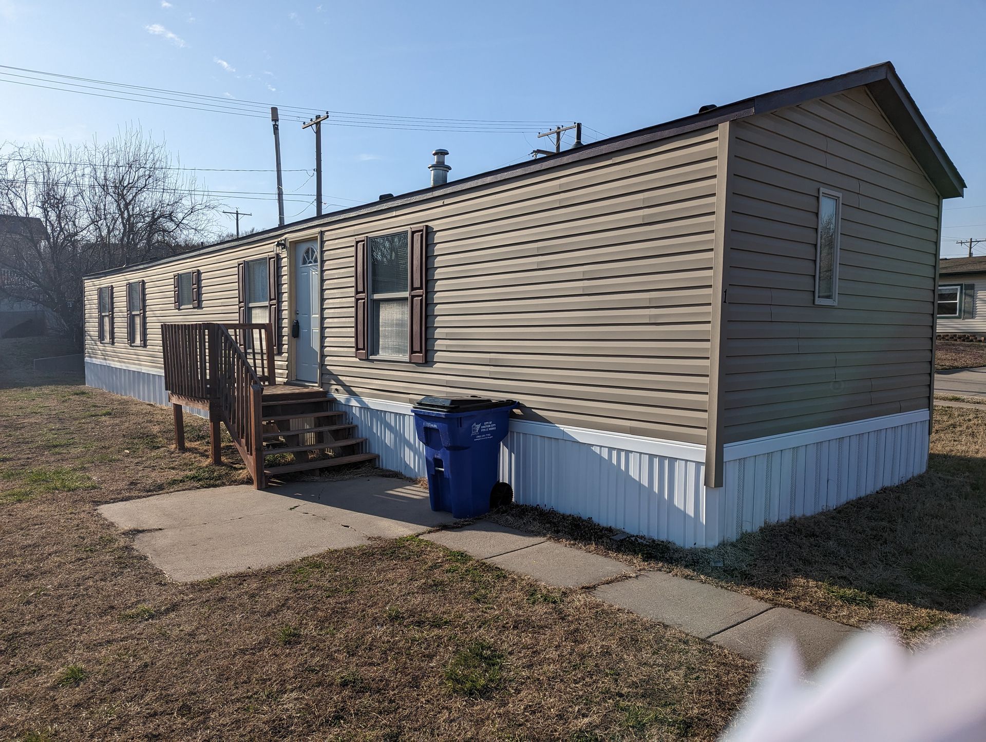 A mobile home with a blue trash can in front of it.