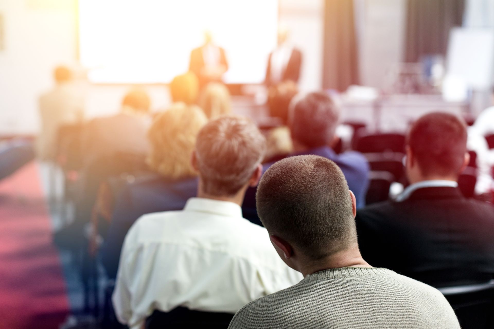 A group of people are sitting in a lecture hall watching a presentation.