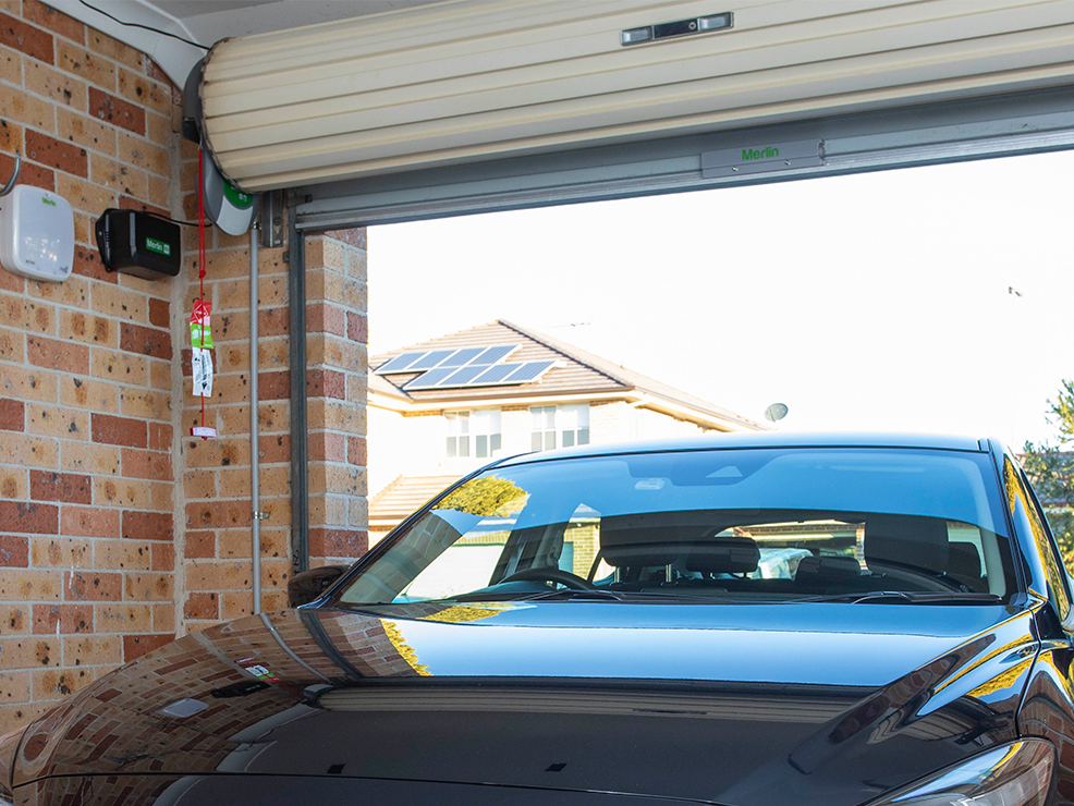 Modern brick garage with a partially open roller garage door and a parked car inside.