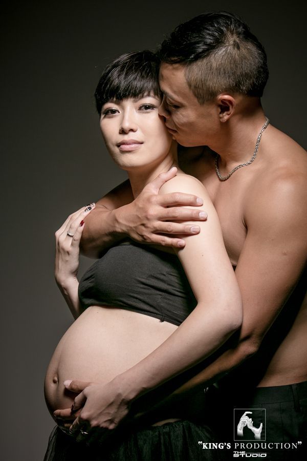 身穿黑色上衣的孕婦擁抱丈夫（工作室拍攝）。他親吻她的臉頰，撫摸她的肚子。
