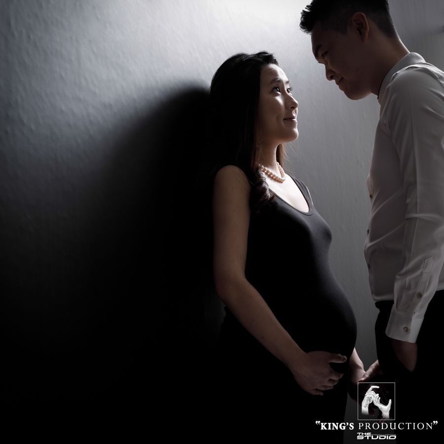 身穿黑色洋裝的孕婦凝視著男人；他們被柔和的燈光照亮。